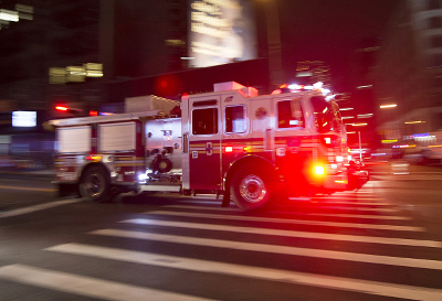 An image of a firetruck driving quickly in a city with its lights on.
